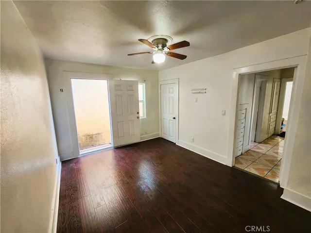a view of an empty room with wooden floor and a ceiling fan