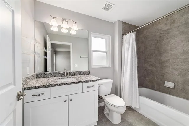 a bathroom with a granite countertop sink a toilet a mirror a bathtub and shower