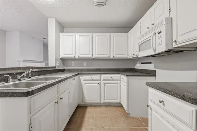 a kitchen with granite countertop white cabinets white appliances and a sink