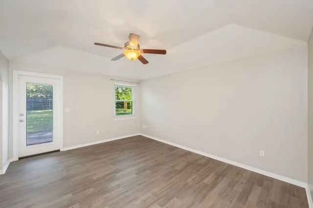 an empty room with wooden floor ceiling fan and windows