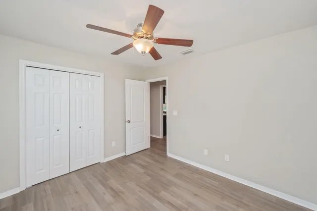 a view of an empty room with wooden floor and a ceiling fan