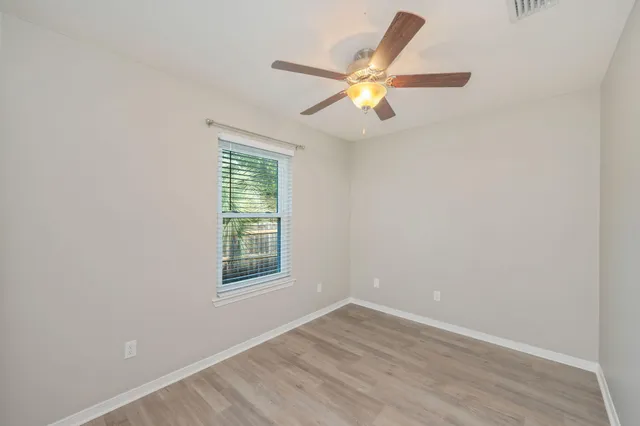 an empty room with wooden floor fan and windows