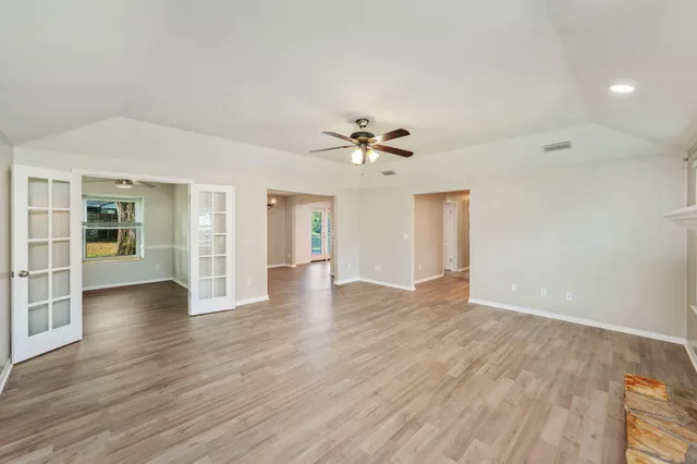 a view of an empty room with wooden floor and a ceiling fan
