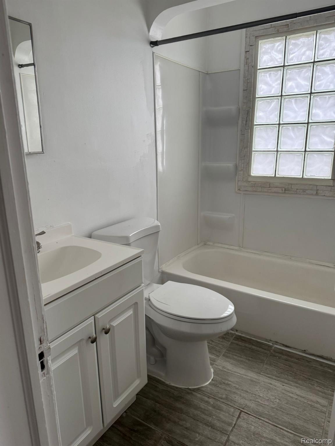 19706 Moross Road Detroit, MI 48224 - Photo 7 of 13 Bathroom featuring a white vanity with panel cabinetry, a white toilet, and a white tub with integrated shelving