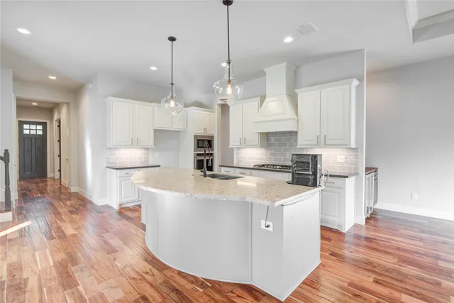 a large kitchen with stainless steel appliances granite countertop a sink a stove a refrigerator and island with wooden floor