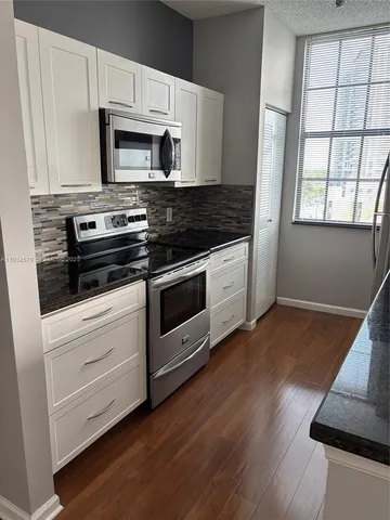 a kitchen with granite countertop wooden floors appliances and cabinets