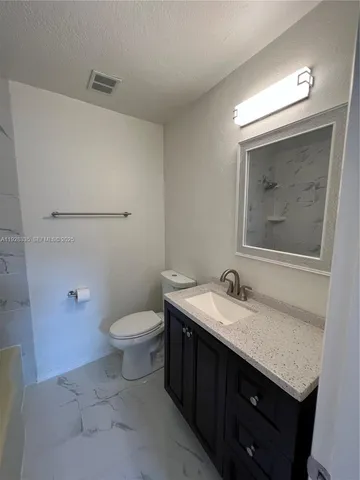a bathroom with a granite countertop sink vanity mirror and toilet
