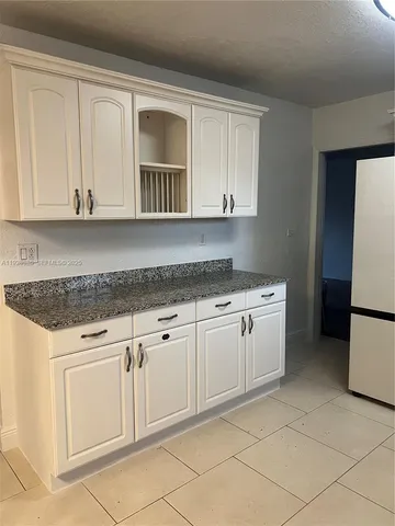 a kitchen with granite countertop white cabinets and refrigerator
