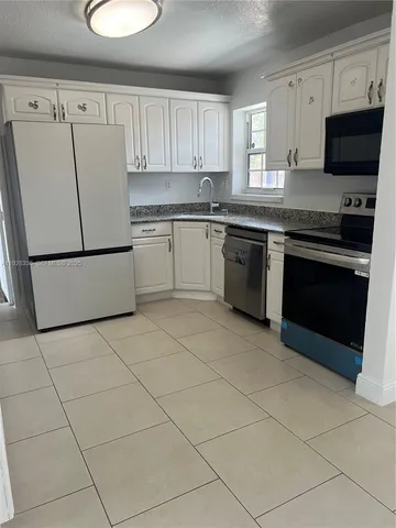 a white kitchen with granite countertop a stove top oven a sink a microwave and a refrigerator