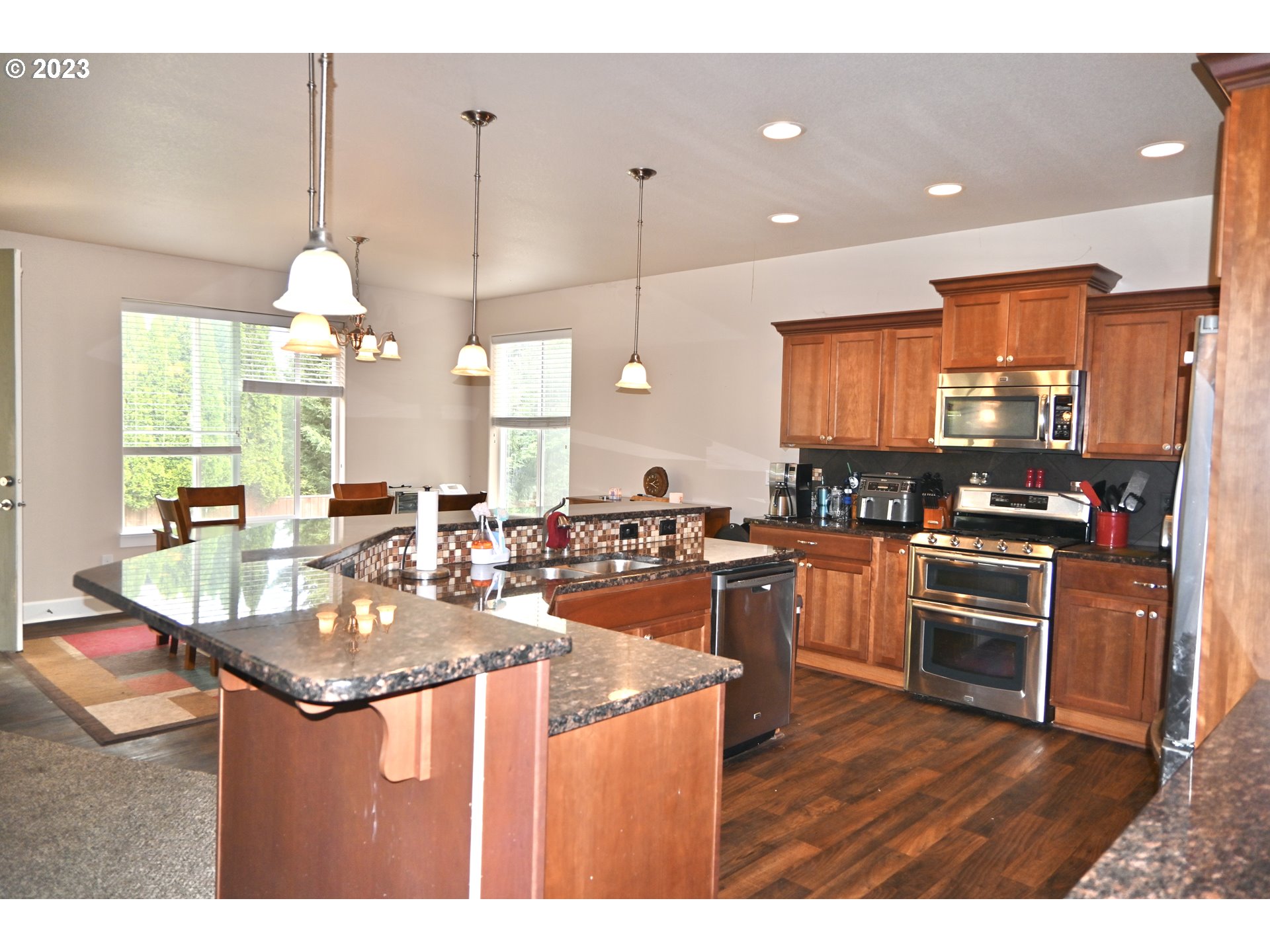 3623 Comiskey Street Forest Grove, OR 97116 - Photo 9 of 43 a kitchen with stainless steel appliances kitchen island granite countertop a sink dishwasher a stove and a dining table with wooden floor