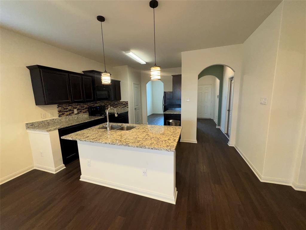 14360 Riata Lane Dallas, TX 75253 - Photo 6 of 16 Kitchen featuring an island with a sink, dark wood-finish cabinetry, light-toned countertops, and a patterned backsplash