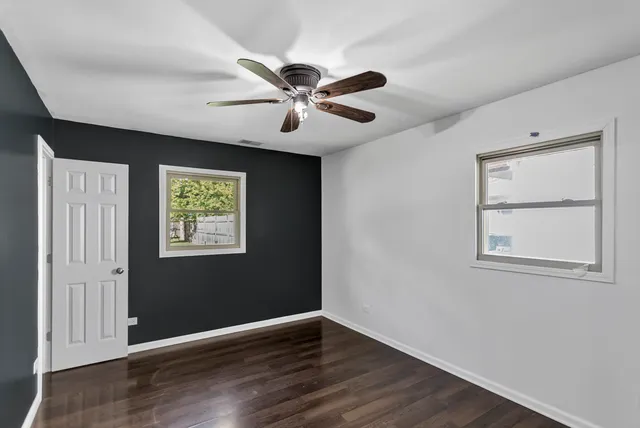an empty room with wooden floor chandelier fan and windows