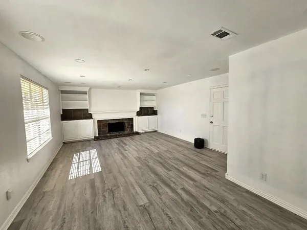 an empty room with wooden floor fireplace and windows