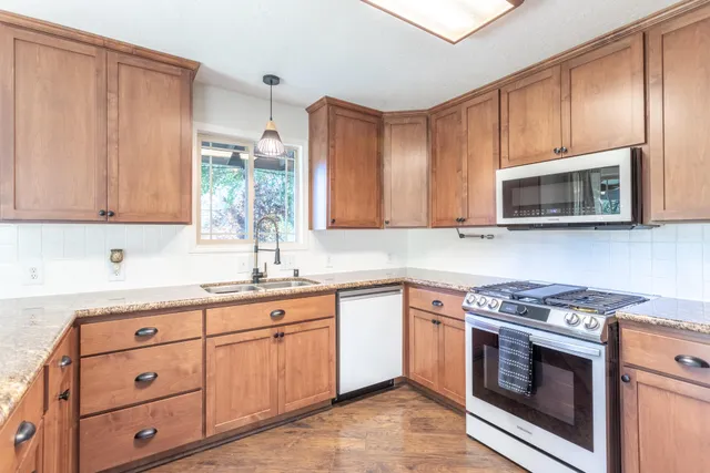 a living room with stainless steel appliances granite countertop a refrigerator a sink dishwasher a stove with wooden cabinets and floor