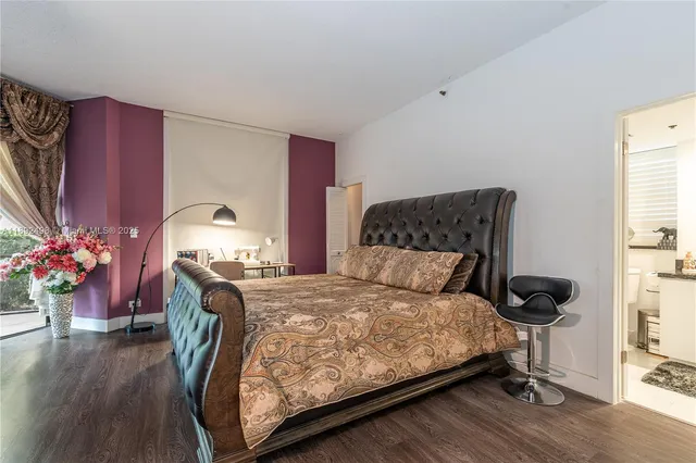 a bedroom with a bed potted plant on dresser and a wooden floor