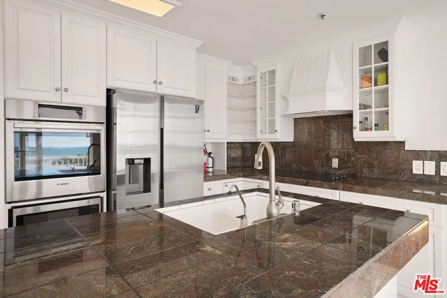 a kitchen with granite countertop a refrigerator a stove and white cabinets with wooden floor