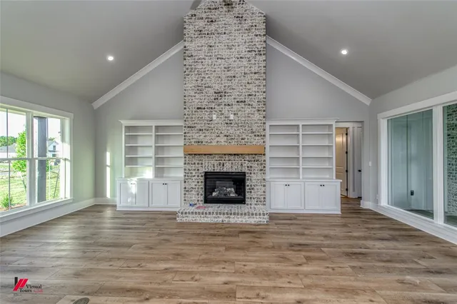 a view of an empty room with wooden floor fireplace and a window