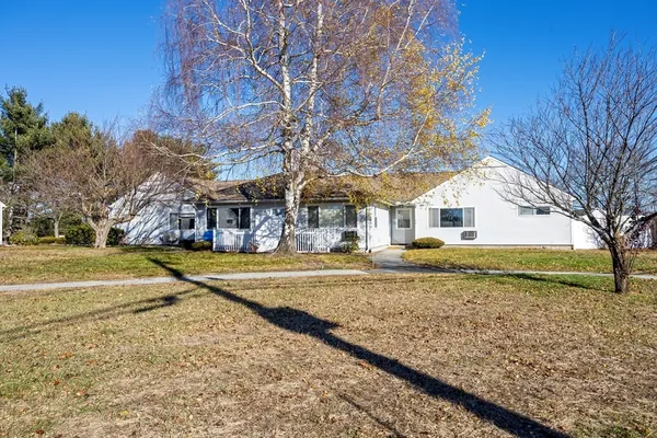 a view of a white house next to a yard with a large tree