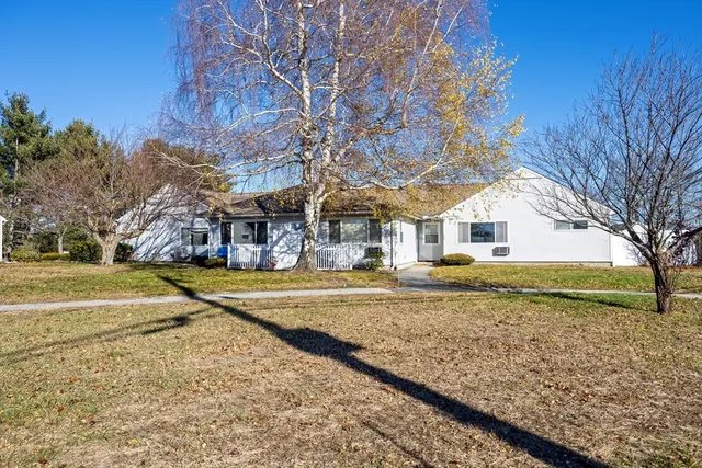 a view of a white house next to a yard with a large tree