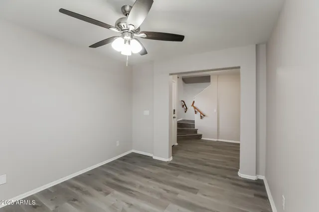a view of an empty room with wooden floor and a ceiling fan