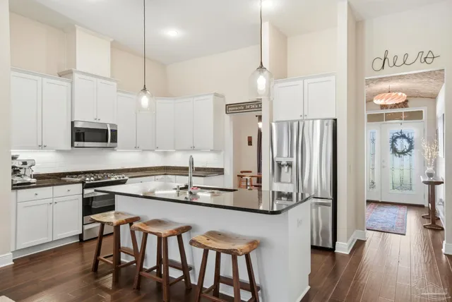 a kitchen with stainless steel appliances kitchen island granite countertop a refrigerator a stove and white cabinets with wooden floor