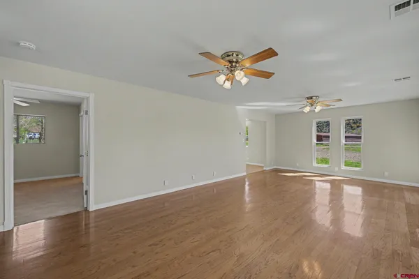 an empty room with wooden floor chandelier fan and windows