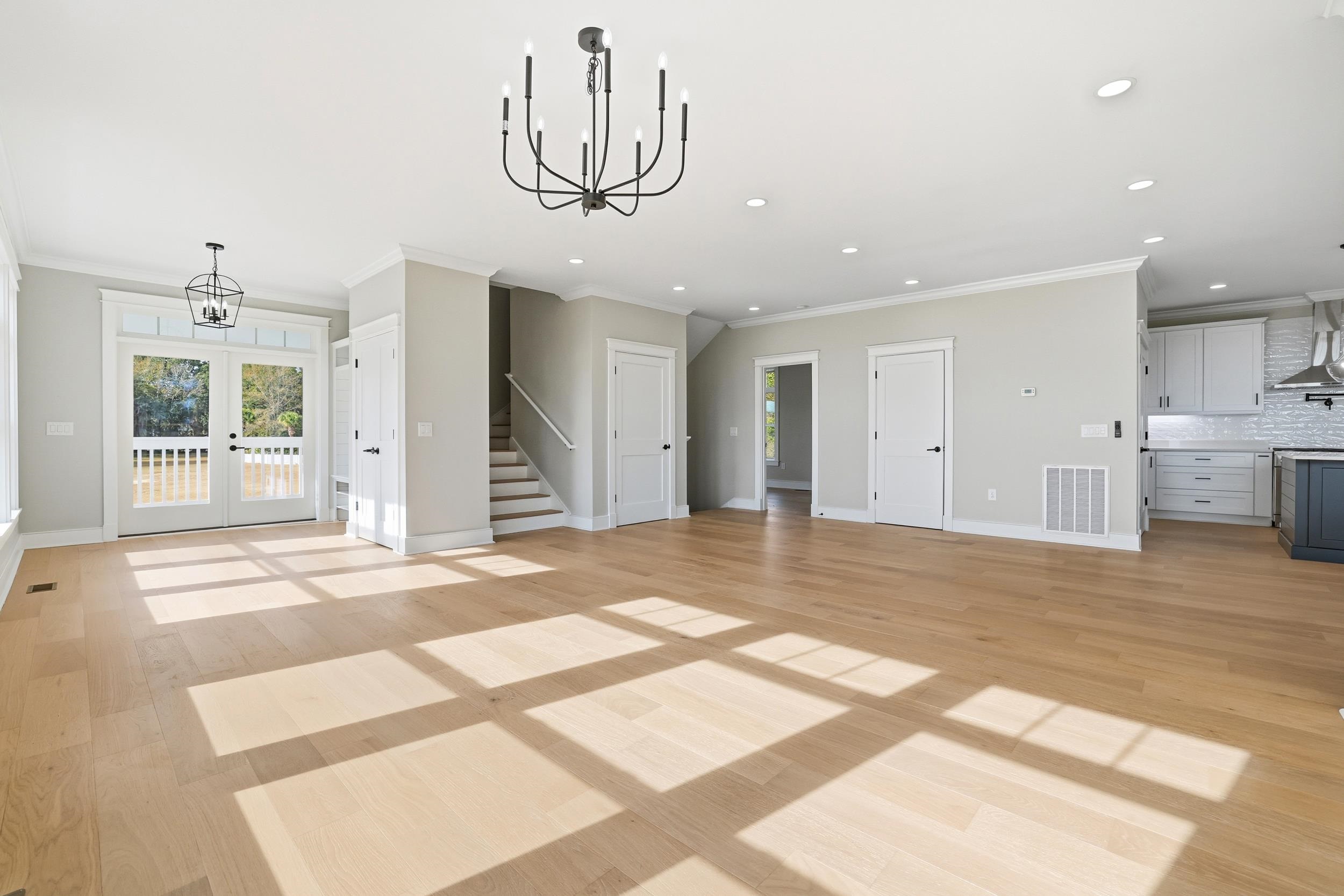 145 Oak Bay Drive Georgetown, SC 29440 - Photo 7 of 39 Unfurnished living room featuring a chandelier, crown molding, french doors, light wood-style floors, and stairs
