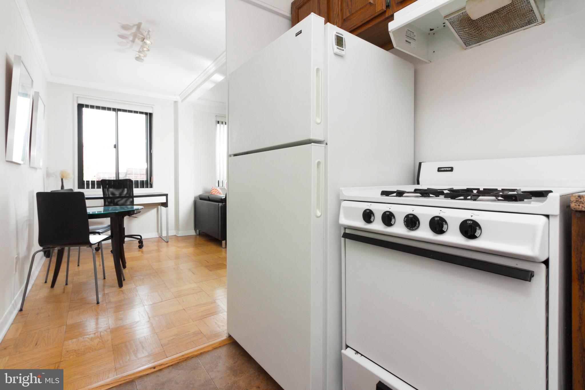 1601 18th Street Northwest, Unit 508 Washington, DC 20009 - Photo 22 of 31 a white kitchen with a stove a refrigerator and a dining table with wooden floor