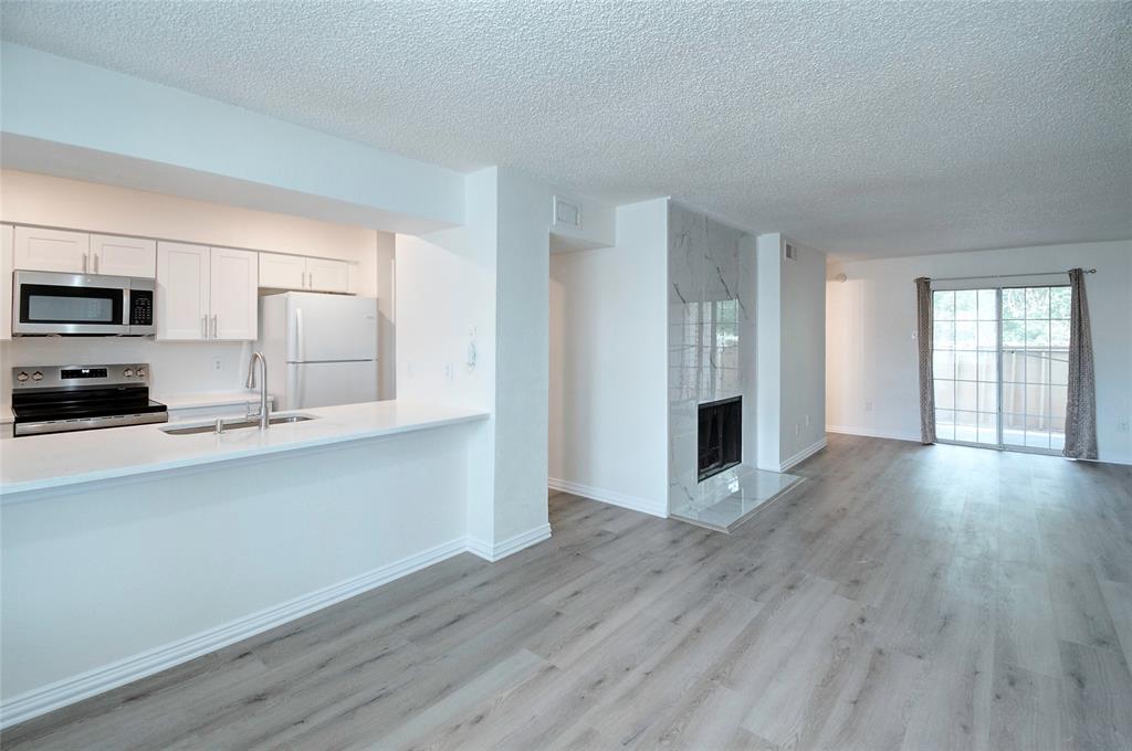 12484 Abrams Road, Unit 1802 Dallas, TX 75243 - Photo 1 of 1 Kitchen with white cabinetry, light wood-type flooring, appliances with stainless steel finishes, a tile fireplace, and a textured ceiling