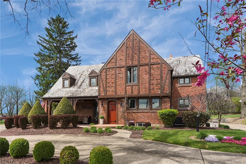 Stunning Tudor-style brick home with timeless curb appeal, featuring a large governor’s driveway, manicured landscaping, and inviting covered front porch.
