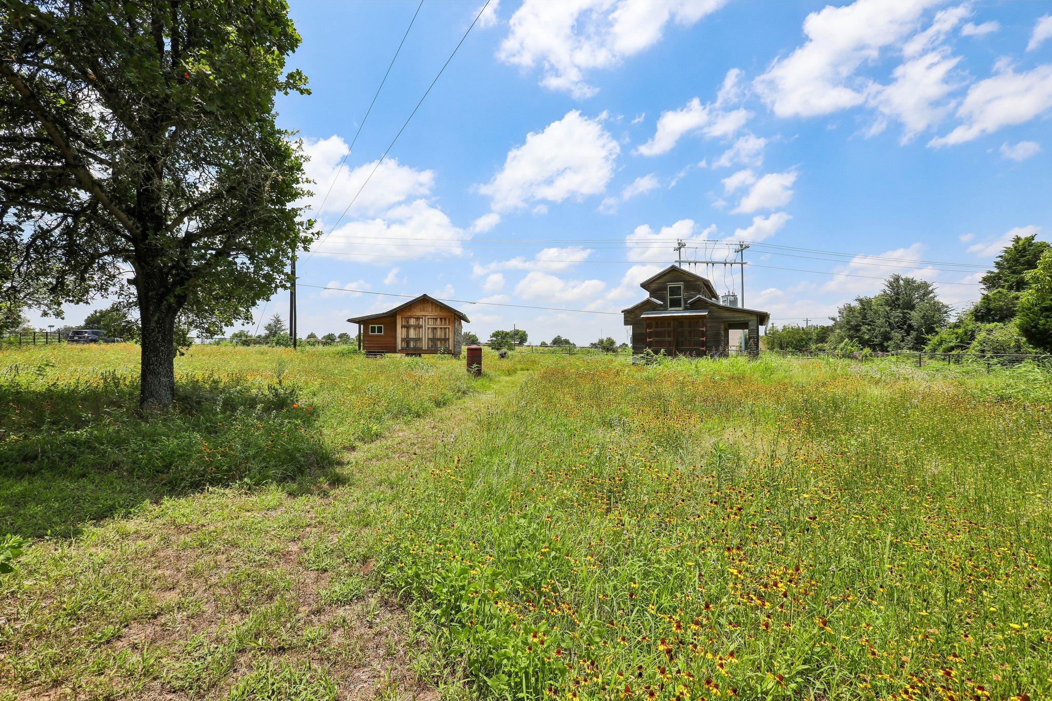 2089 Farm To Market Road 1704 Elgin, TX 78621 - Photo 25 of 31 Two rustic structures sit amidst a vibrant field of wildflowers, framed by mature trees and open skies.