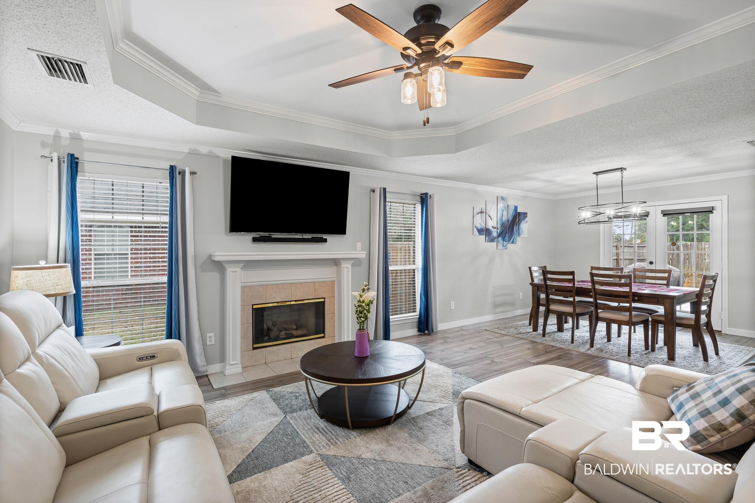 9590 Polo Pl Court Mobile, AL 36695 - Photo 2 of 22 Living room featuring crown molding, a tiled fireplace, wood finished floors, a ceiling fan, and a tray ceiling