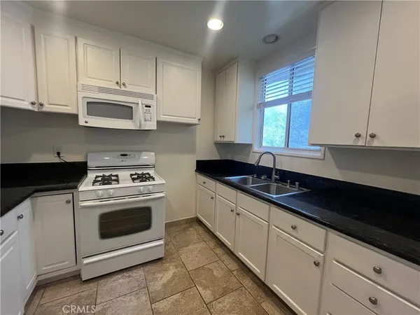 a kitchen with granite countertop white cabinets sink and white appliances