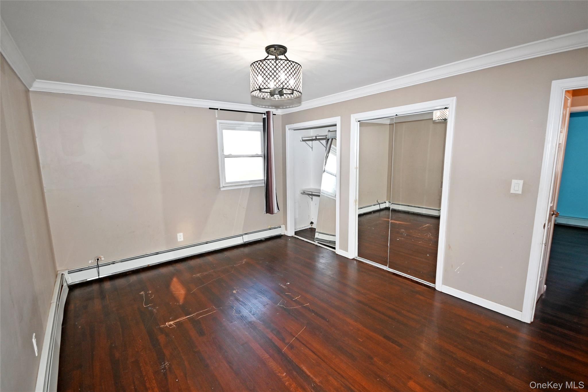 89 Osborne Road West Hempstead, NY 11552 - Photo 15 of 50 Unfurnished bedroom with two closets, dark wood-type flooring, ornamental molding, and a baseboard heating unit