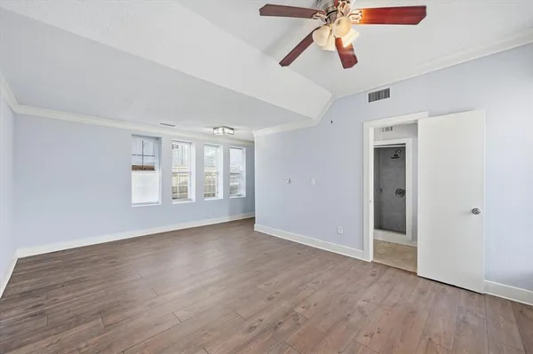 a view of an empty room with wooden floor and a ceiling fan