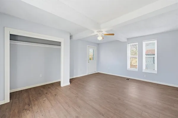 an empty room with wooden floor ceiling fan and windows