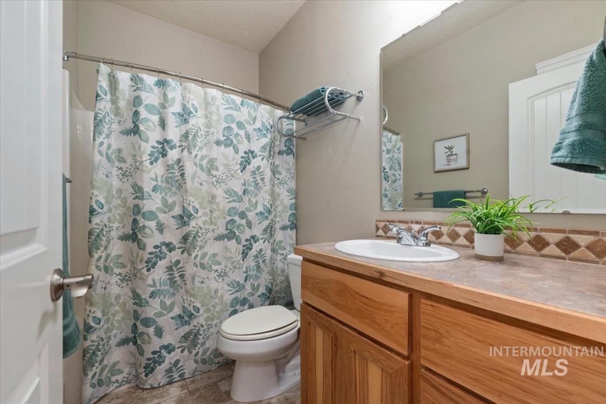 640 Southwest Miner Street Mountain Home, ID 83647 - Photo 11 of 35 Bathroom featuring a wood-finish vanity with an integrated sink, a rectangular mirror, and a tile backsplash