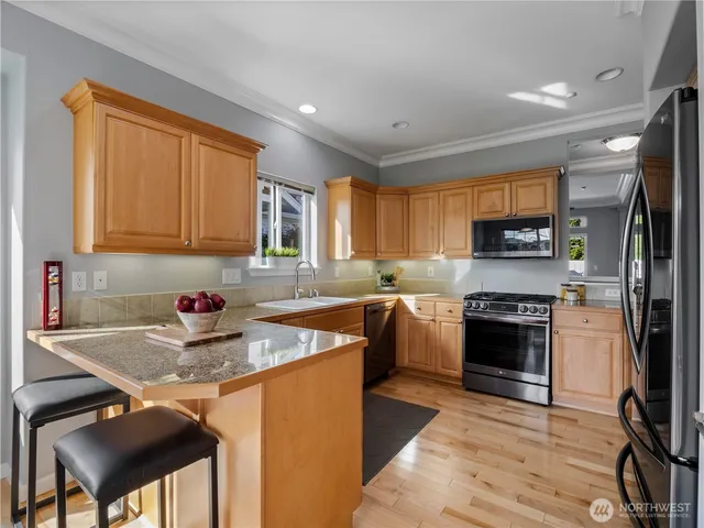 a kitchen with stainless steel appliances granite countertop a stove top oven a sink dishwasher a dining table and chairs with wooden floor