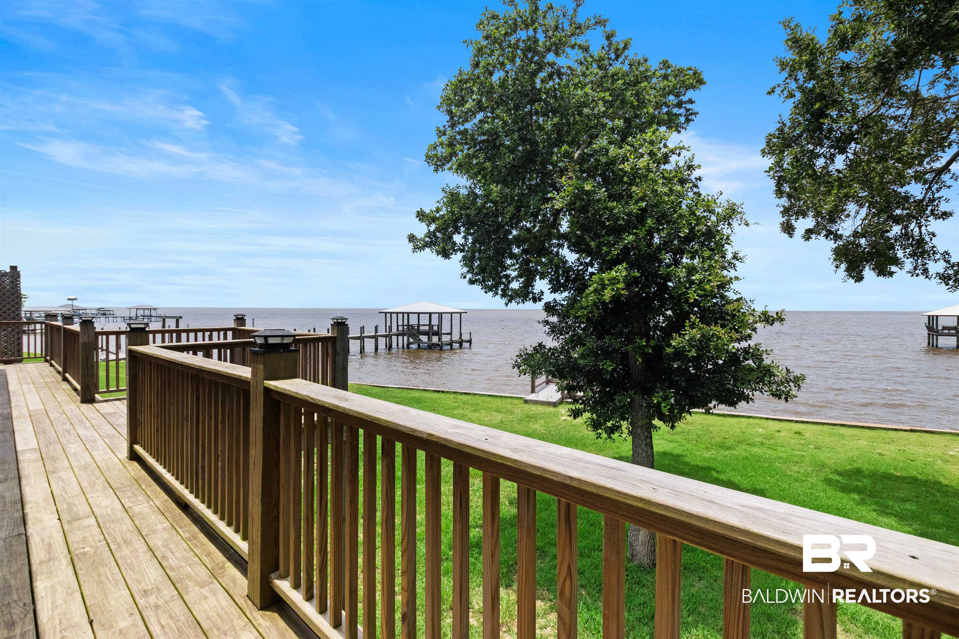 9581 South Bay Street Foley, AL 36535 - Photo 32 of 44 Waterfront property featuring an expansive wood deck, a boat dock with a covered slip, mature trees, and a manicured lawn