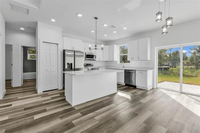 a kitchen with stainless steel appliances kitchen island granite countertop a refrigerator oven a sink and a dining table with wooden floor