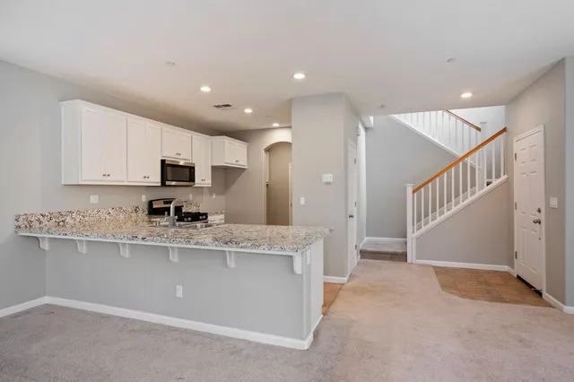 a kitchen with stainless steel appliances granite countertop a refrigerator a sink dishwasher a stove and white cabinets with wooden floor