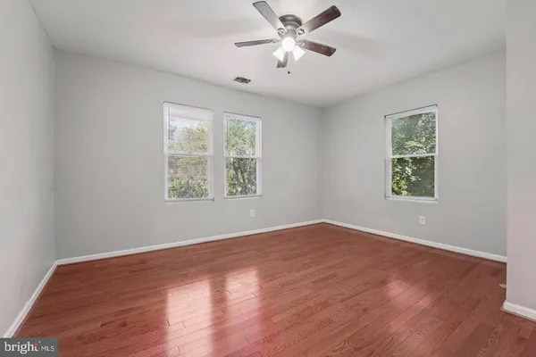 an empty room with wooden floor chandelier fan and windows