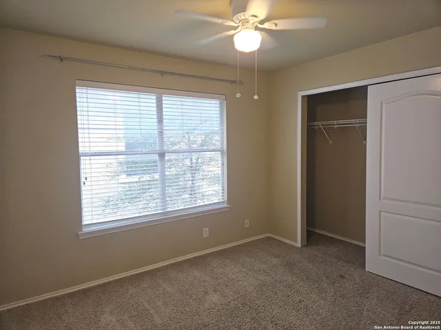 an empty room with chandelier fan and kitchen view