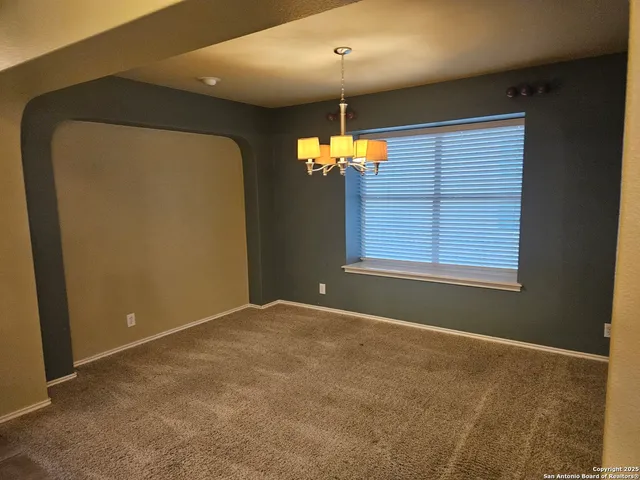 a view of an empty room with window and chandelier fan