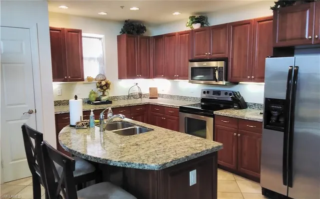 a kitchen with kitchen island granite countertop a sink dishwasher stove and refrigerator with wooden cabinets