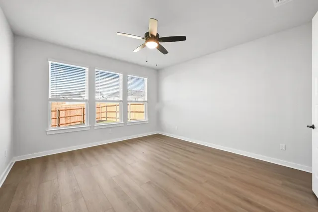 an empty room with wooden floor ceiling fan and windows