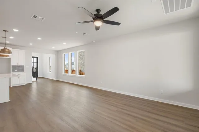 a view of an empty room with wooden floor and a ceiling fan