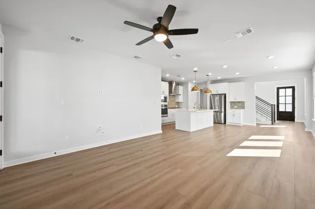 a view of an empty room with wooden floor and a ceiling fan