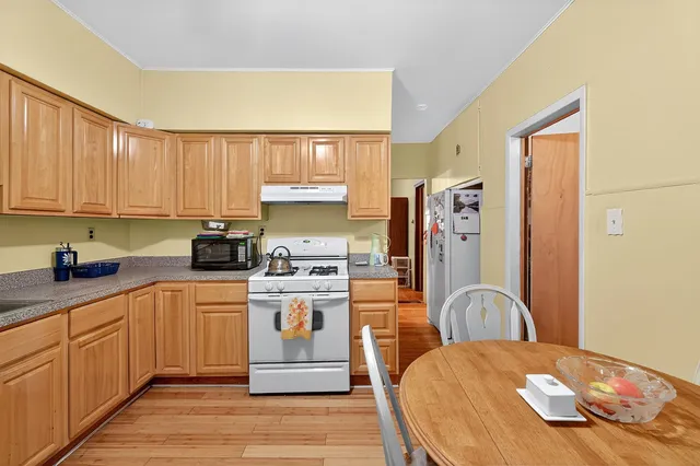 a kitchen with stainless steel appliances kitchen island granite countertop a refrigerator a sink dishwasher and white cabinets with wooden floor