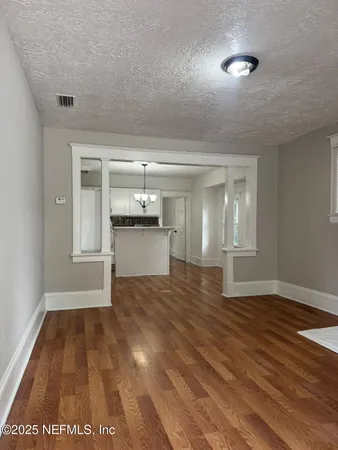 a view of empty room with wooden floor and kitchen